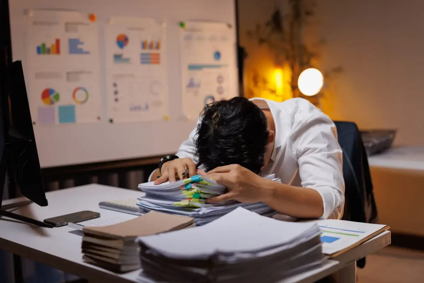 Overworked business person exhausted by workload, sleeping at desk during late night in office
