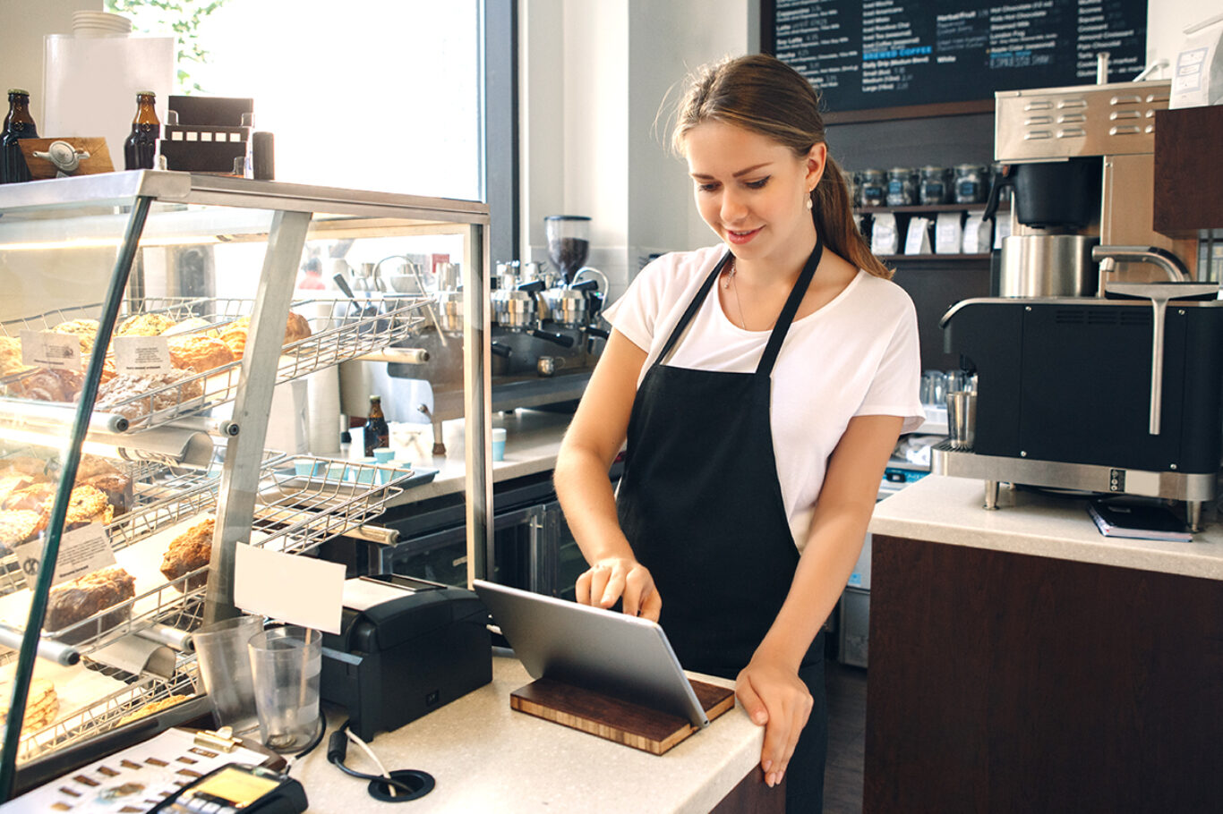 Portrait of young caucasian female woman cashier. Seller using touch pad for accepting client customer payment. Small business of coffee shop cafeteria.