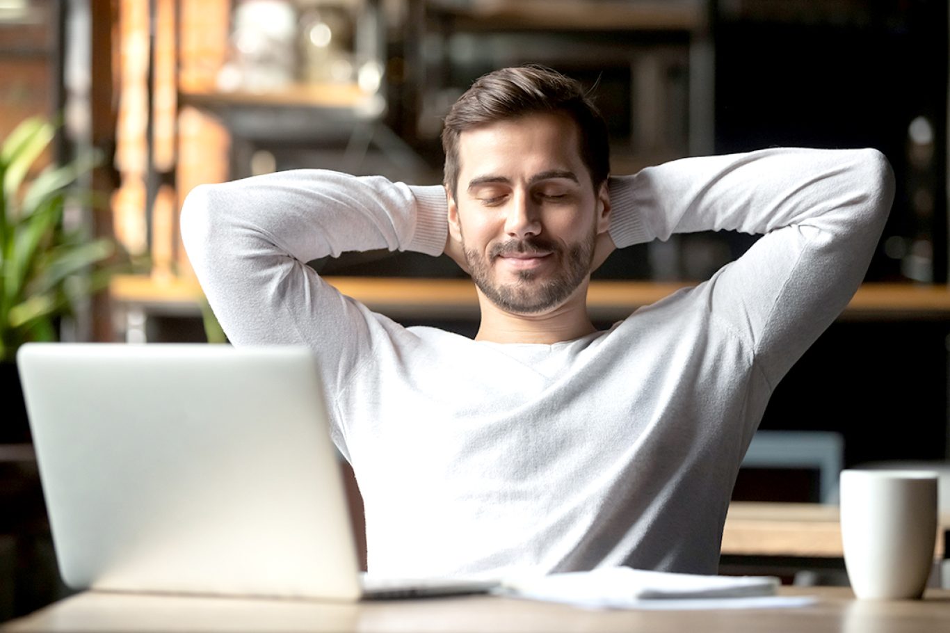 Relaxed happy businessman student worker lounge at work desk cafe table meditating, positive calm man relax break hold hand behind head dream rest from computer stretch feel no stress peace of mind