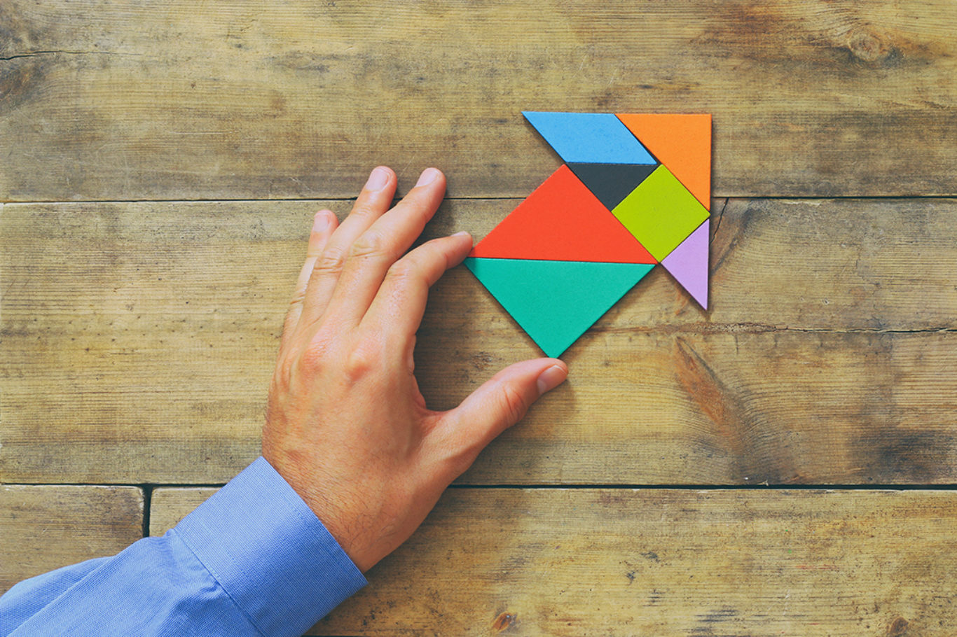man's hand pointing at arrow made from square tangram puzzle, wooden background
