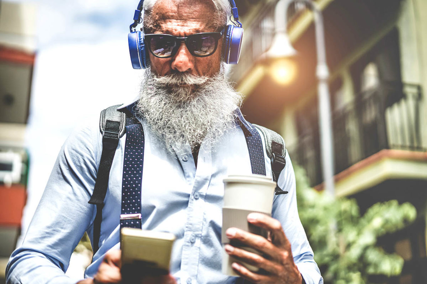 Happy senior man listening music playlist app and drinking coffee at early morning time - Technology, trendy lifestyle,  and joyful elderly lifestyle concept - Focus on headphones